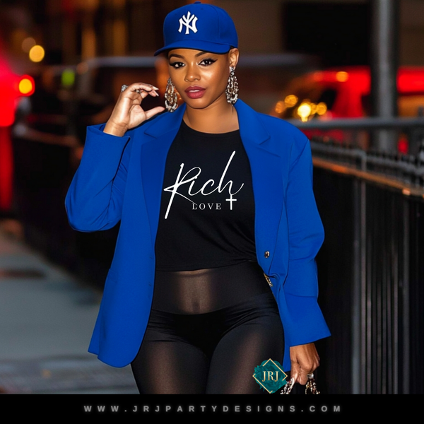 Black Christian t-shirt with white Rich Love graphic text, faith-based inspirational unisex streetwear design.
A woman wearing a blue blazer, black pants, and a New York Yankees cap, with 'RICH LOVE' printed on a black t-shirt underneath.